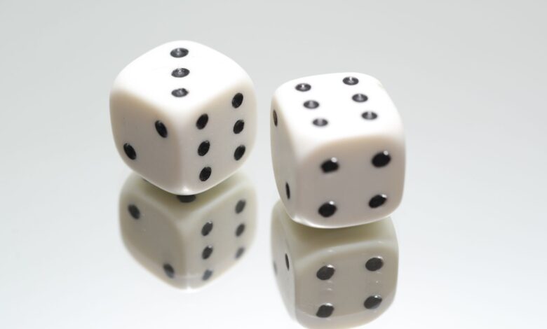 A close-up view of two white dice with reflection on a smooth white surface, symbolizing luck and chance.