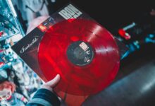 From above crop person holding red vinyl disc with inscription cover in music shop