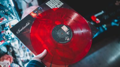 From above crop person holding red vinyl disc with inscription cover in music shop