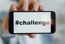 Close-up of a hand holding a smartphone displaying a '#challenge' hashtag.