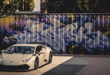 A sleek luxury sports car parked in front of a vibrant graffiti wall under bright daylight.