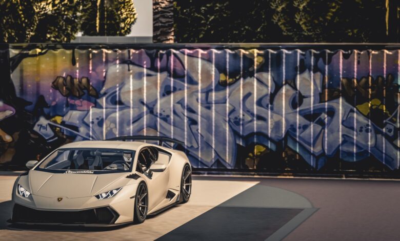 A sleek luxury sports car parked in front of a vibrant graffiti wall under bright daylight.