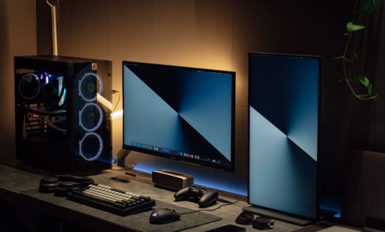 Modern dual monitor PC setup with tech gadgets on a sleek desk in a dimly lit room.