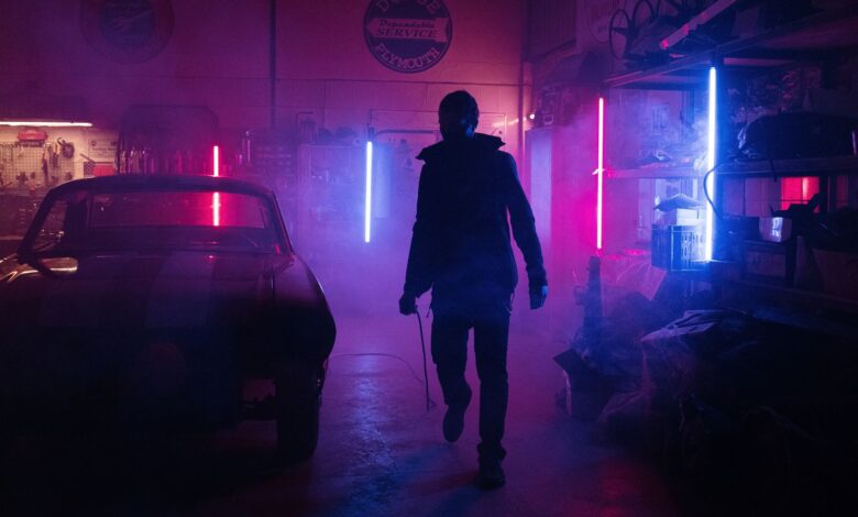 A mechanic in a neon-lit garage works amidst vibrant pink and blue lights, creating a moody, cyberpunk atmosphere.