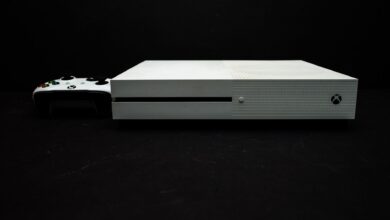 Close-up of a white gaming console with a black controller on a dark background.