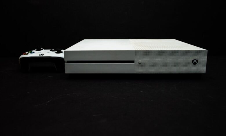 Close-up of a white gaming console with a black controller on a dark background.