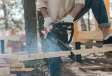 Outdoor scene of a man skillfully using a chainsaw on wood, showcasing carpentry expertise.