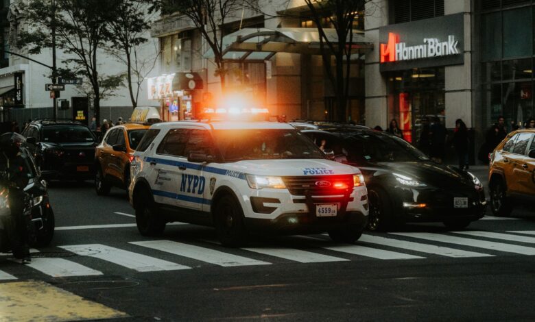 NYPD patrol car with flashing lights in downtown city traffic scene.