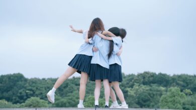 Three teenage girls in school uniforms hugging outdoors on a cloudy day.