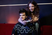 Two young adults having fun playing video games on a couch, smiling and holding a game controller.