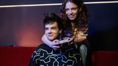 Two young adults having fun playing video games on a couch, smiling and holding a game controller.