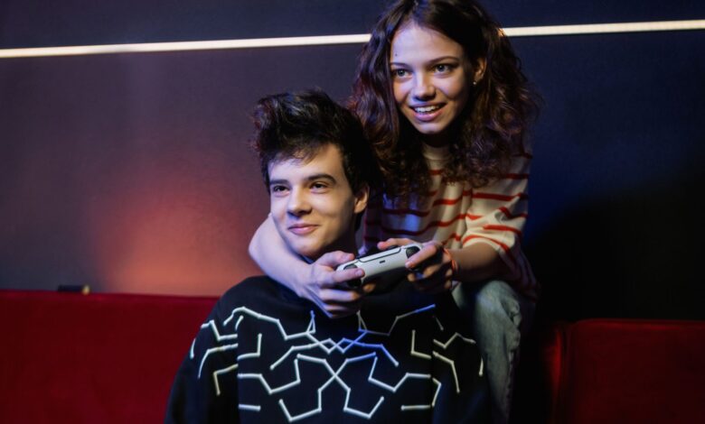 Two young adults having fun playing video games on a couch, smiling and holding a game controller.