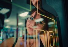 A woman reflected in arcade machine glass, enveloped in neon lights.