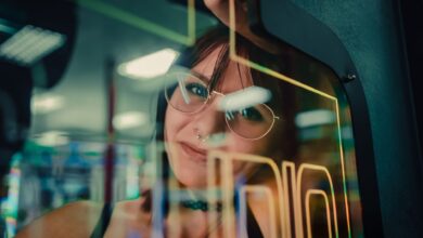 A woman reflected in arcade machine glass, enveloped in neon lights.