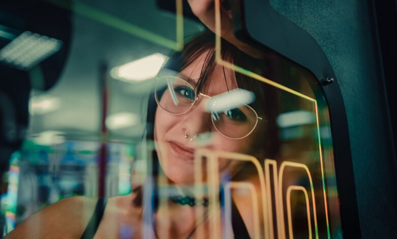 A woman reflected in arcade machine glass, enveloped in neon lights.