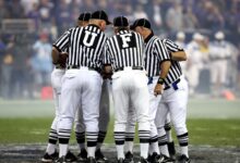 Group of sports officials in striped uniforms discussing on a football field.