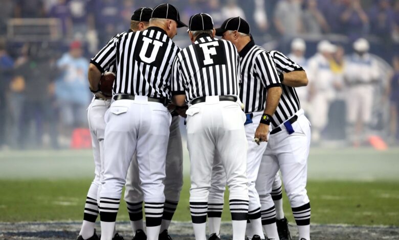 Group of sports officials in striped uniforms discussing on a football field.