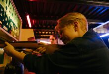 Group of teenagers at an arcade playing a retro shooting game and having fun together.