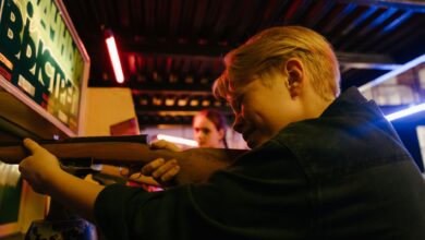 Group of teenagers at an arcade playing a retro shooting game and having fun together.