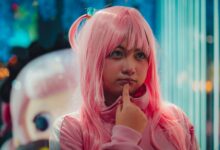 Close-up of young woman in pink wig and costume, pondering indoors.