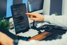 A programmer working on code with a laptop and monitor setup in an office.