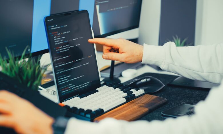A programmer working on code with a laptop and monitor setup in an office.