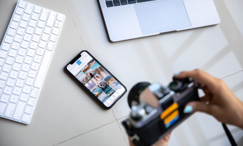 Person using vintage camera with smartphone and laptop in creative setup.