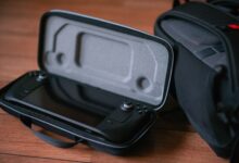 A close-up of a portable gaming device in a protective case next to a bag on a wooden floor.