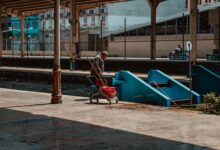 A man cleaning a railroad station platform with cleaning equipment, under a roofed area.