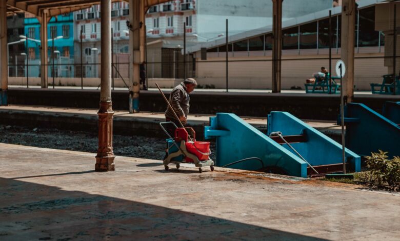 A man cleaning a railroad station platform with cleaning equipment, under a roofed area.