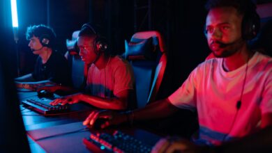 Three gamers immersed in a competitive setting with neon lighting, using keyboards and wearing headsets.