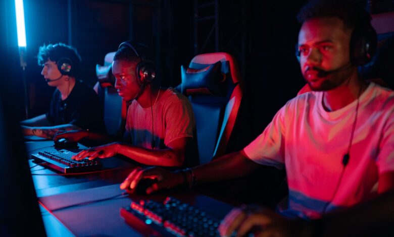 Three gamers immersed in a competitive setting with neon lighting, using keyboards and wearing headsets.