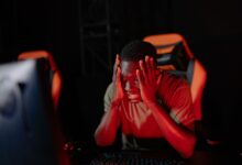 A man intensely reacts to a game loss at his computer in a dimly lit gaming room.