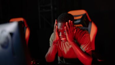 A man intensely reacts to a game loss at his computer in a dimly lit gaming room.
