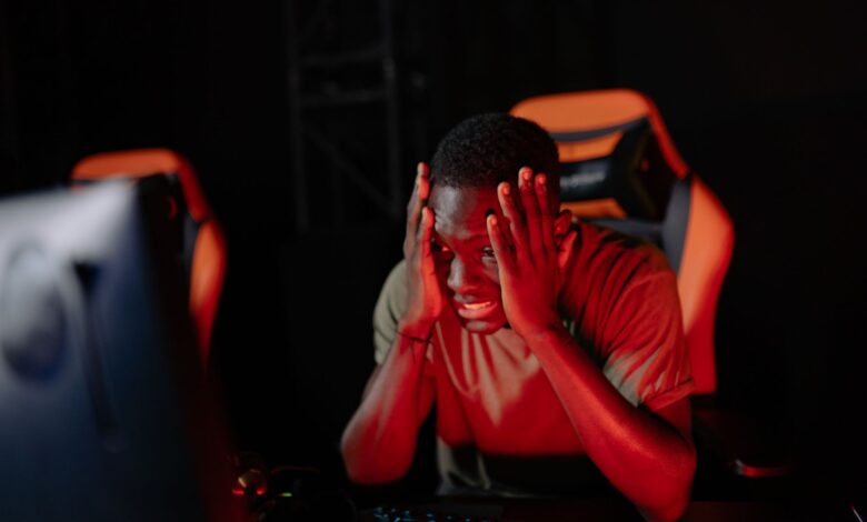A man intensely reacts to a game loss at his computer in a dimly lit gaming room.