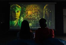 Two people sitting indoors gaming on a large projector screen, enjoying a video game session.