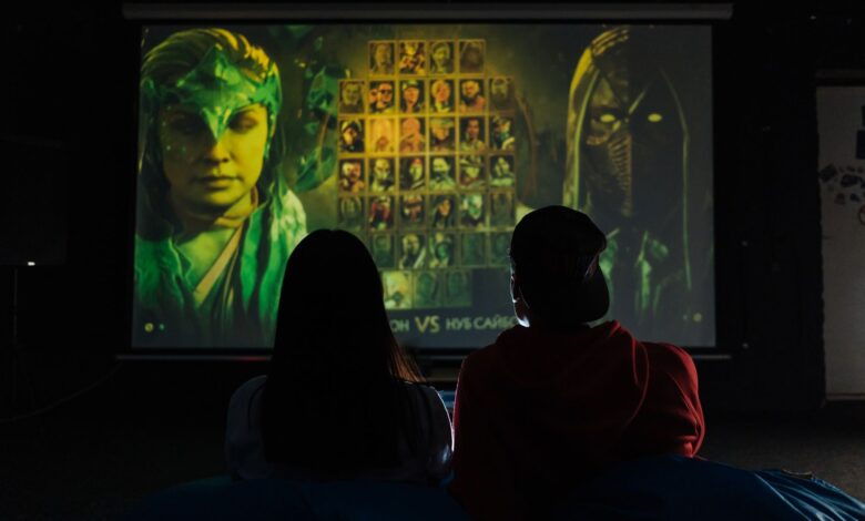 Two people sitting indoors gaming on a large projector screen, enjoying a video game session.