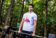A man performs a weightlifting exercise in a forest park, showcasing fitness and strength outdoors.