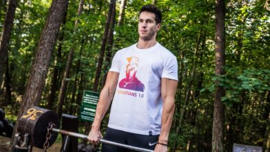 A man performs a weightlifting exercise in a forest park, showcasing fitness and strength outdoors.