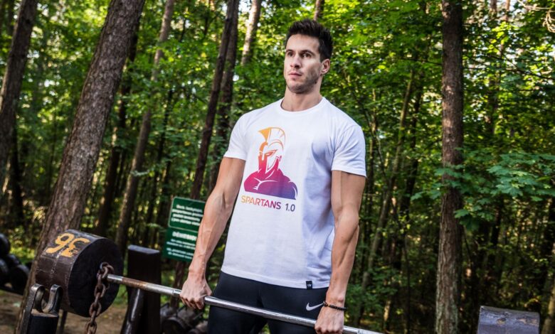A man performs a weightlifting exercise in a forest park, showcasing fitness and strength outdoors.