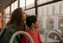 Two young women share an intimate moment on a bus, gazing thoughtfully outside.
