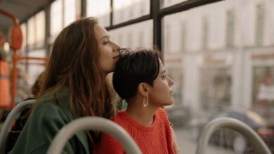 Two young women share an intimate moment on a bus, gazing thoughtfully outside.