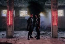 Two models in a dystopian setting with neon lights and smoke, showcasing futuristic fashion.