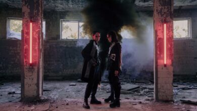 Two models in a dystopian setting with neon lights and smoke, showcasing futuristic fashion.