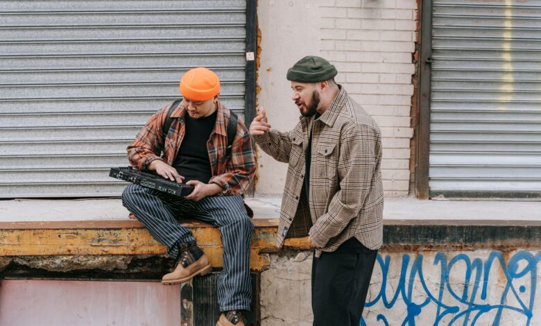 Two men interacting with a synthesizer against an urban backdrop.
