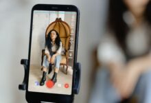 A woman sits in a chair recording a video on her smartphone, showcasing modern vlogging techniques.