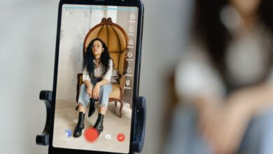 A woman sits in a chair recording a video on her smartphone, showcasing modern vlogging techniques.