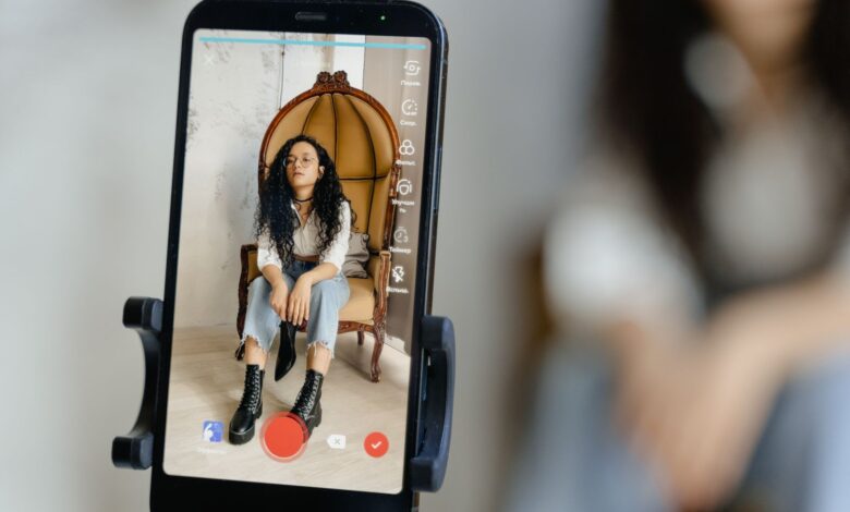 A woman sits in a chair recording a video on her smartphone, showcasing modern vlogging techniques.