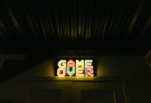 Glowing neon sign with pixelated Game Over text in a dark arcade setting.