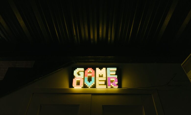 Glowing neon sign with pixelated Game Over text in a dark arcade setting.